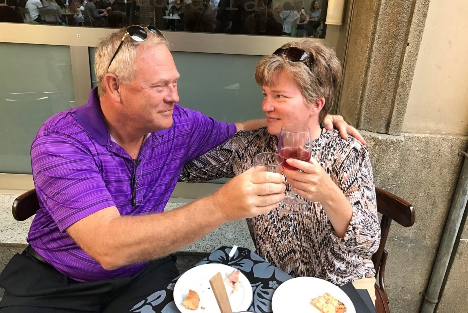 A man and a woman are sitting at a table toasting with wine glasses.