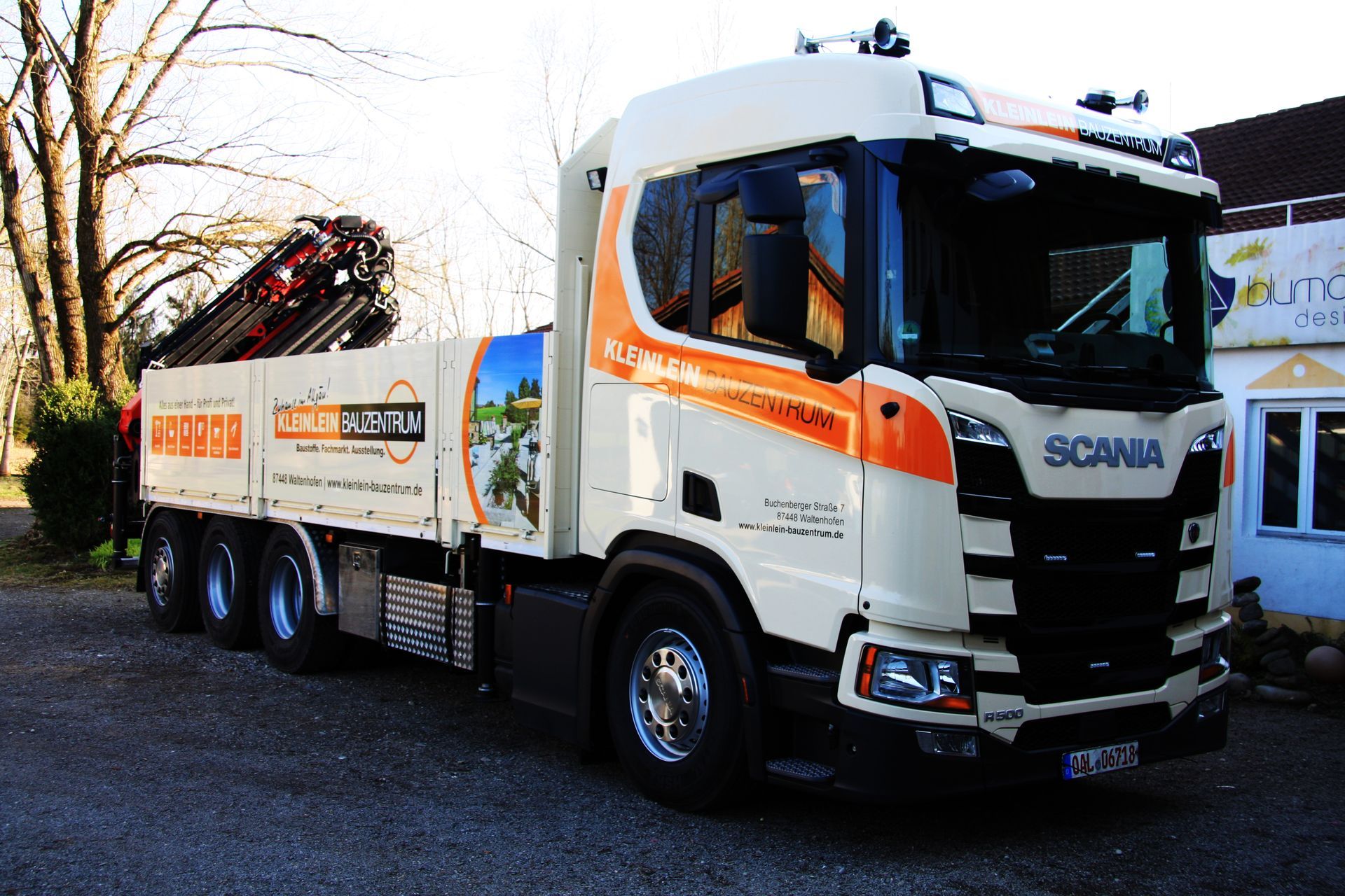 Ein weiß-orangefarbener Scania-Truck steht vor einem Gebäude