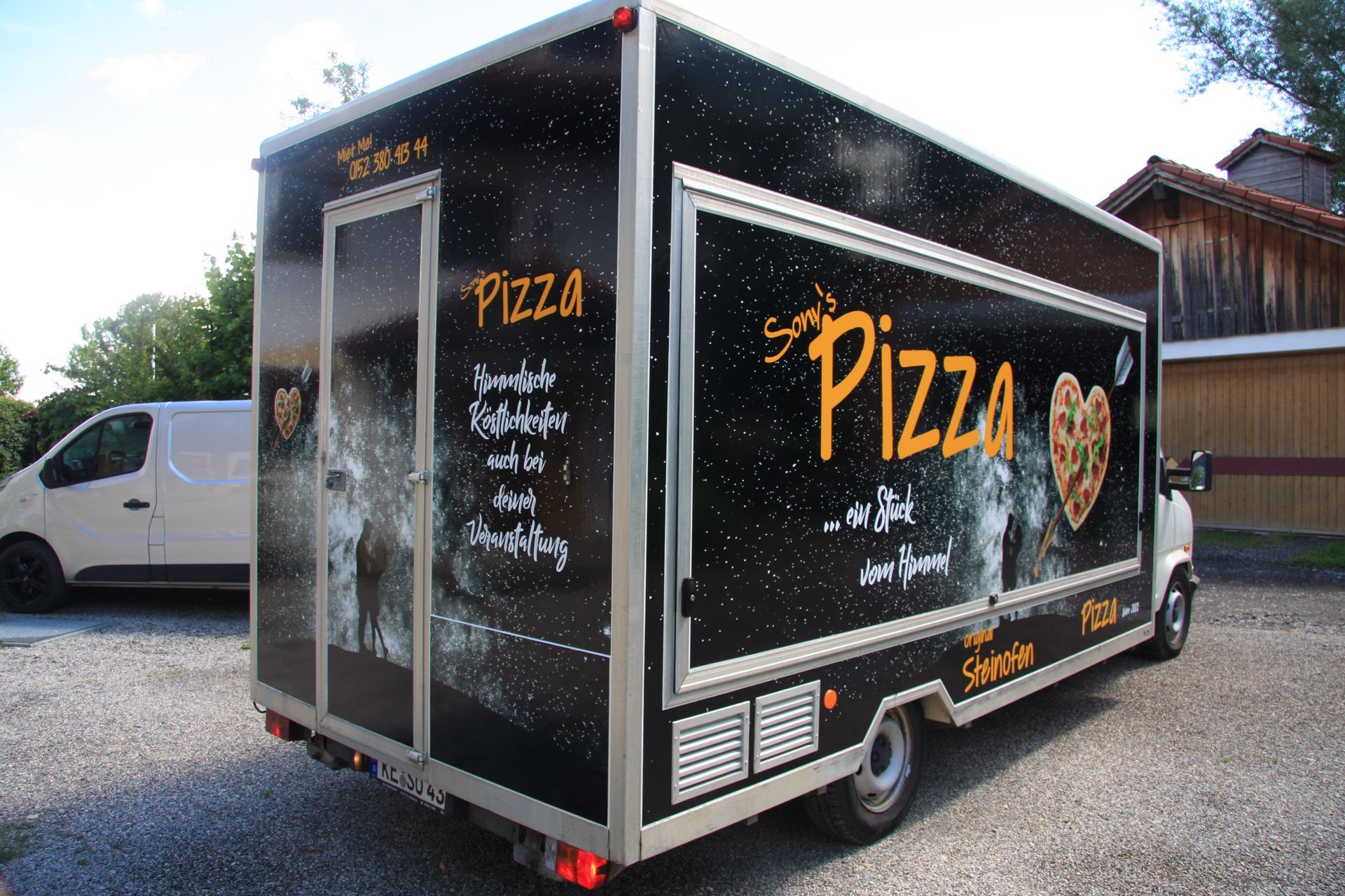 Auf einem Parkplatz steht ein Pizzawagen neben einem weißen Lieferwagen.