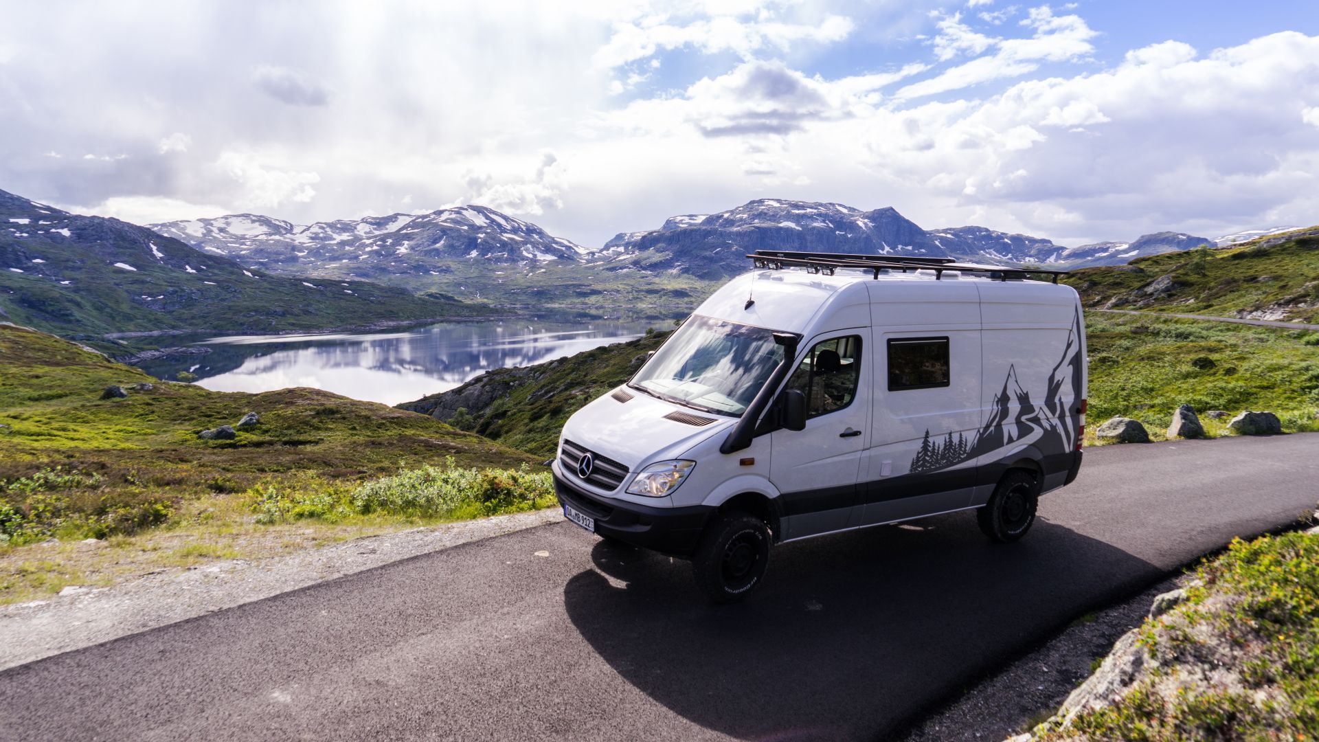 Ein weißer Lieferwagen fährt eine Straße in den Bergen entlang.