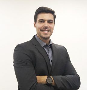 Um homem de terno e gravata posa para uma foto com os braços cruzados.