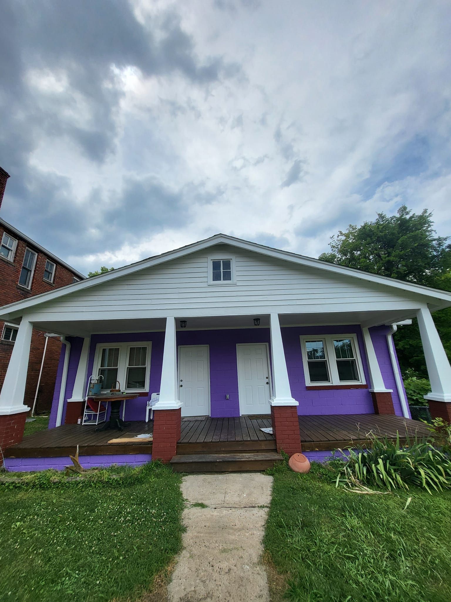 A purple and white house with a porch on a cloudy day.