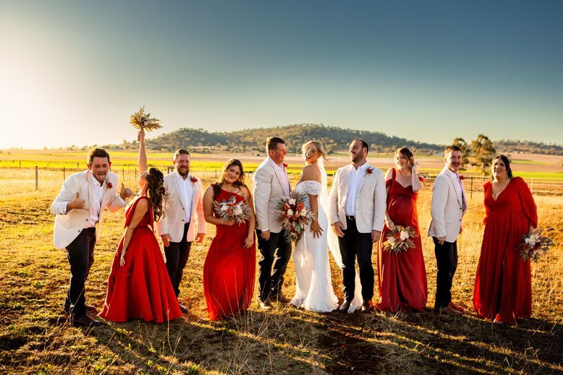 A bride and groom are posing for a picture with their wedding party in a field.