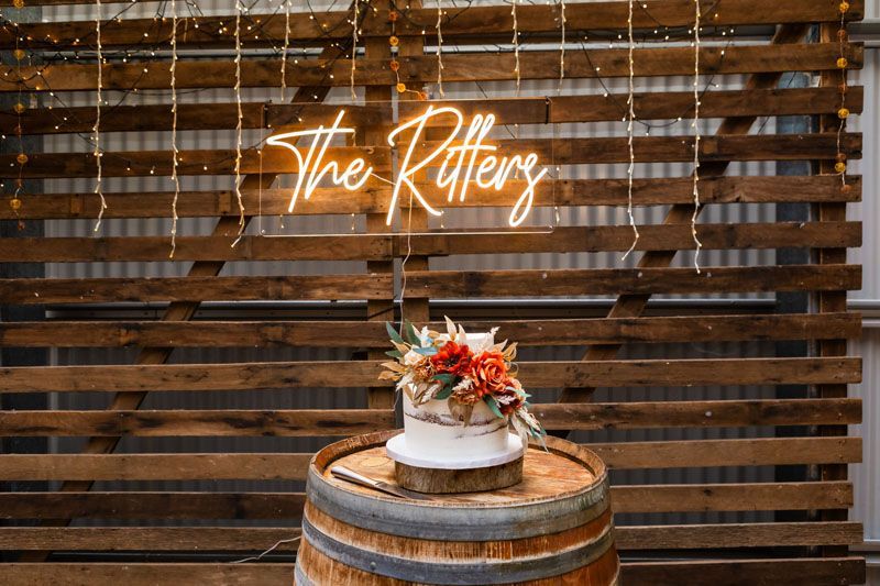 A wedding cake is sitting on top of a wooden barrel in front of a wooden wall.