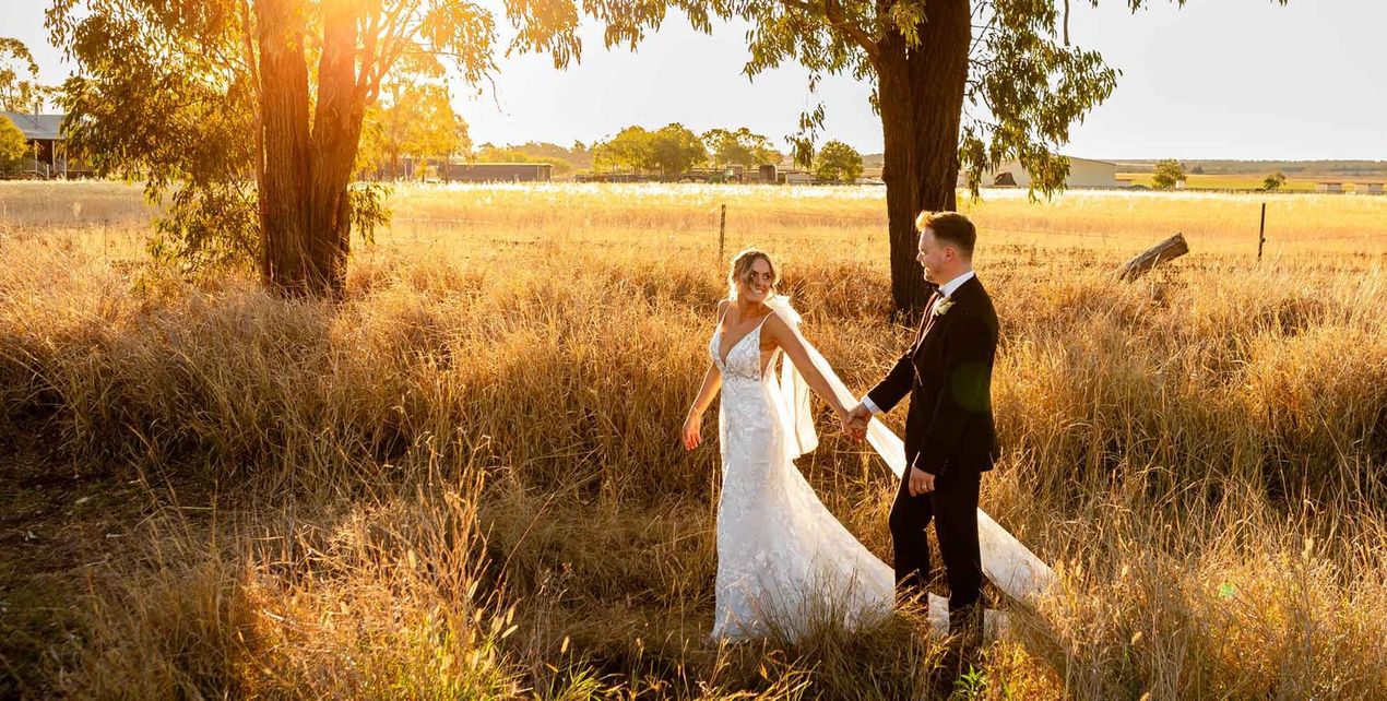 A bride and groom are standing in a field at Aberfeldy Barn,holding hands.