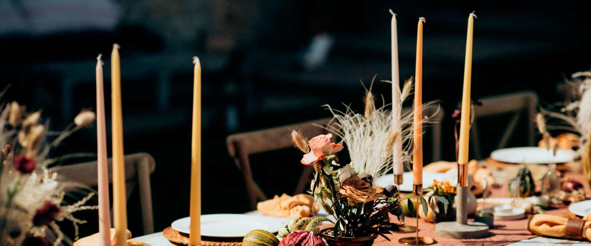 Table setting with tall candles, flowers, and greenery. Warm tones and natural light.