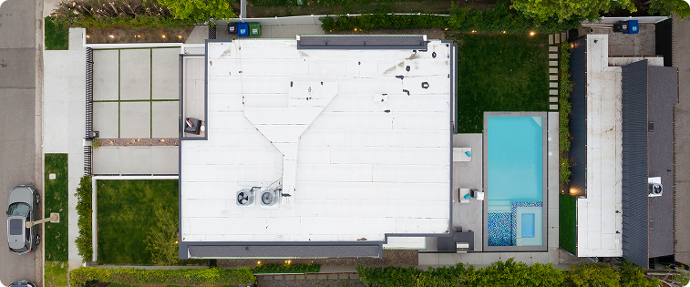 An aerial view of a house with a red roof and a pool in the background.