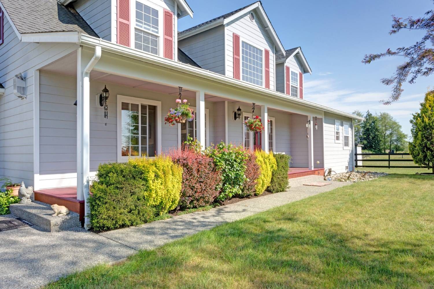A large white house with a porch and a dog in front of it.