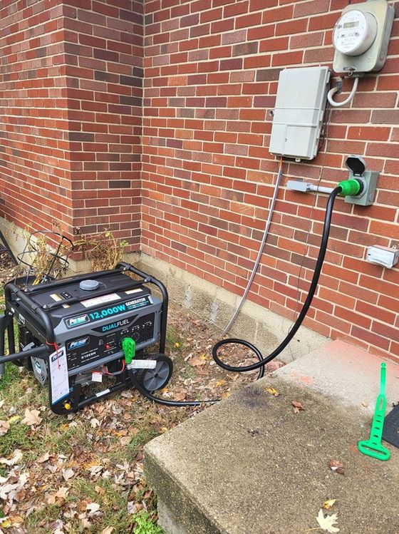 A generator is plugged into an outlet on the side of a brick building.