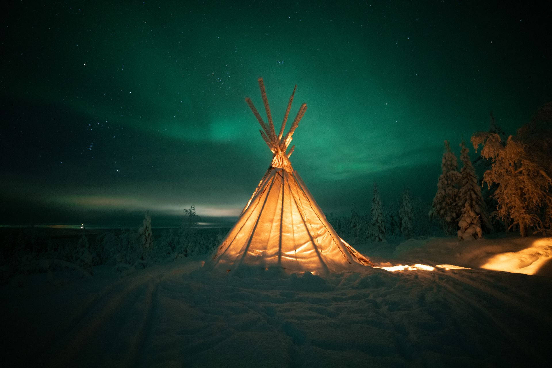 Hut under the Northern Lights surrounded by snowy landscape.