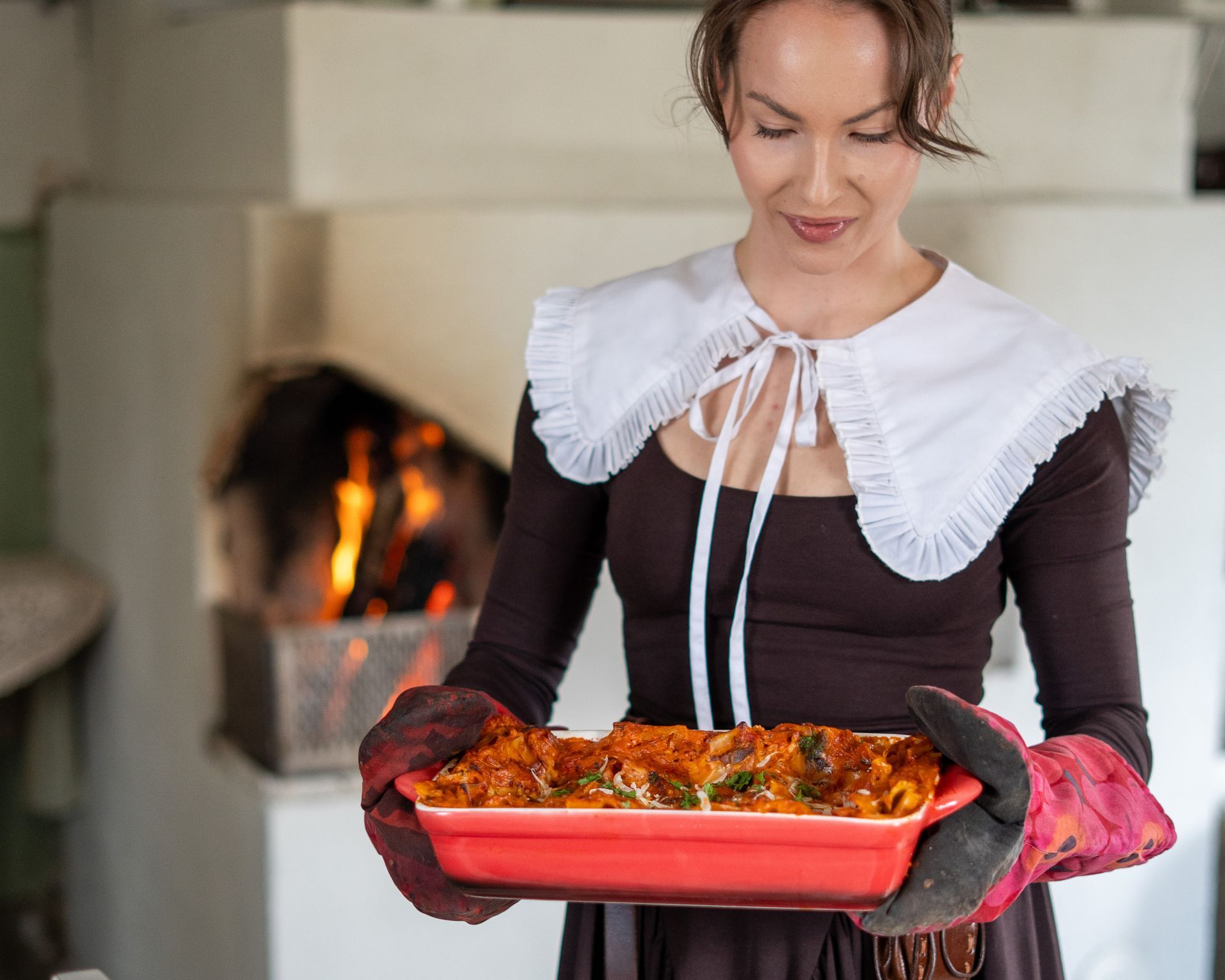 Woman in a vintage dress carrying a traditional Finnish stew fresh from the wooden oven
