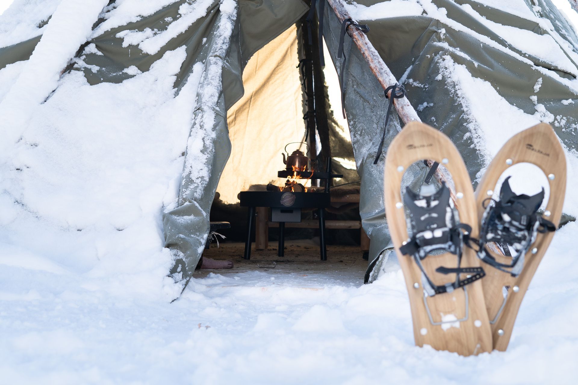 Snowshoes in front of a traditional hut with a fire inside. 