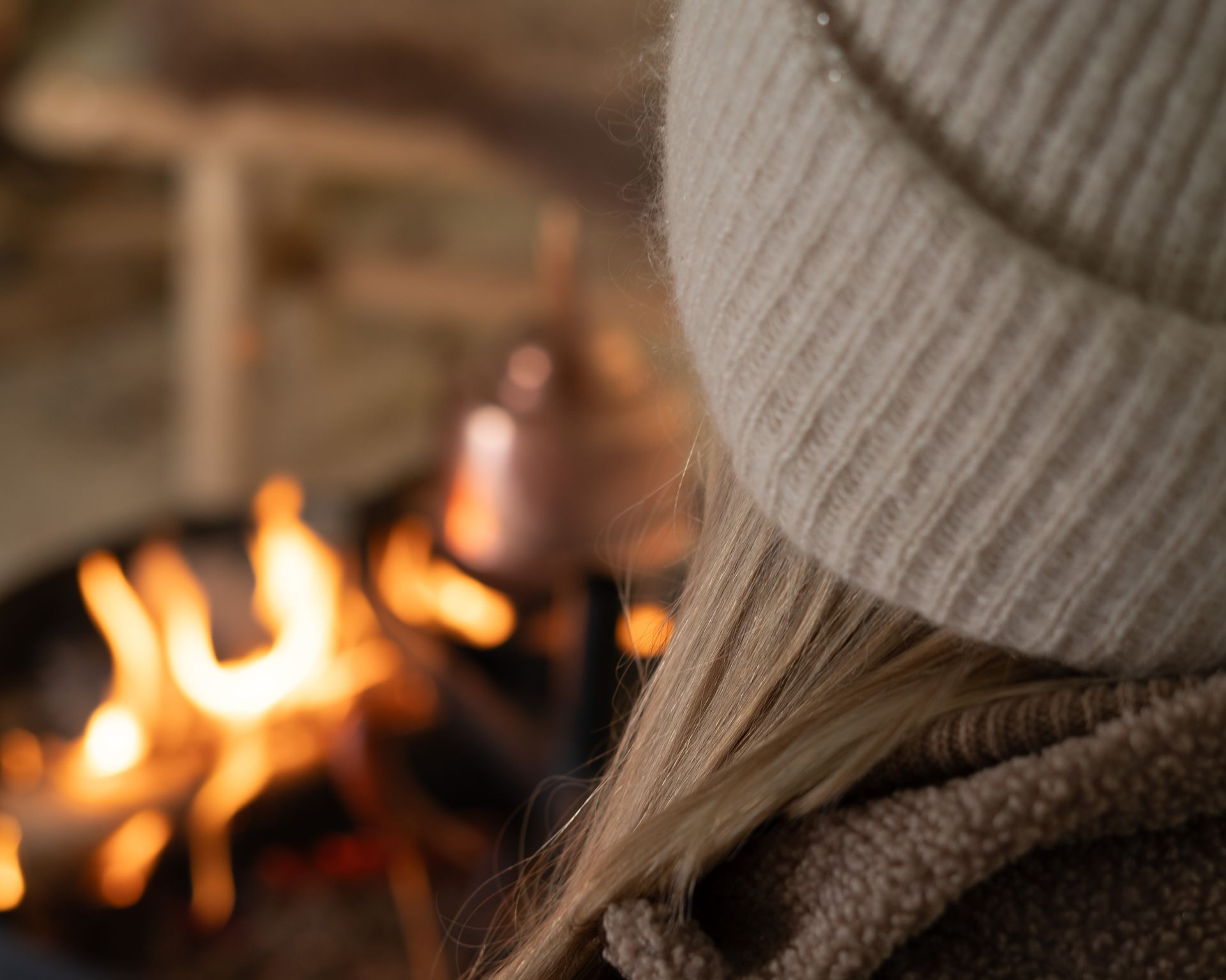 Woman sitting in front of a fire and a copper pot brewing coffee.