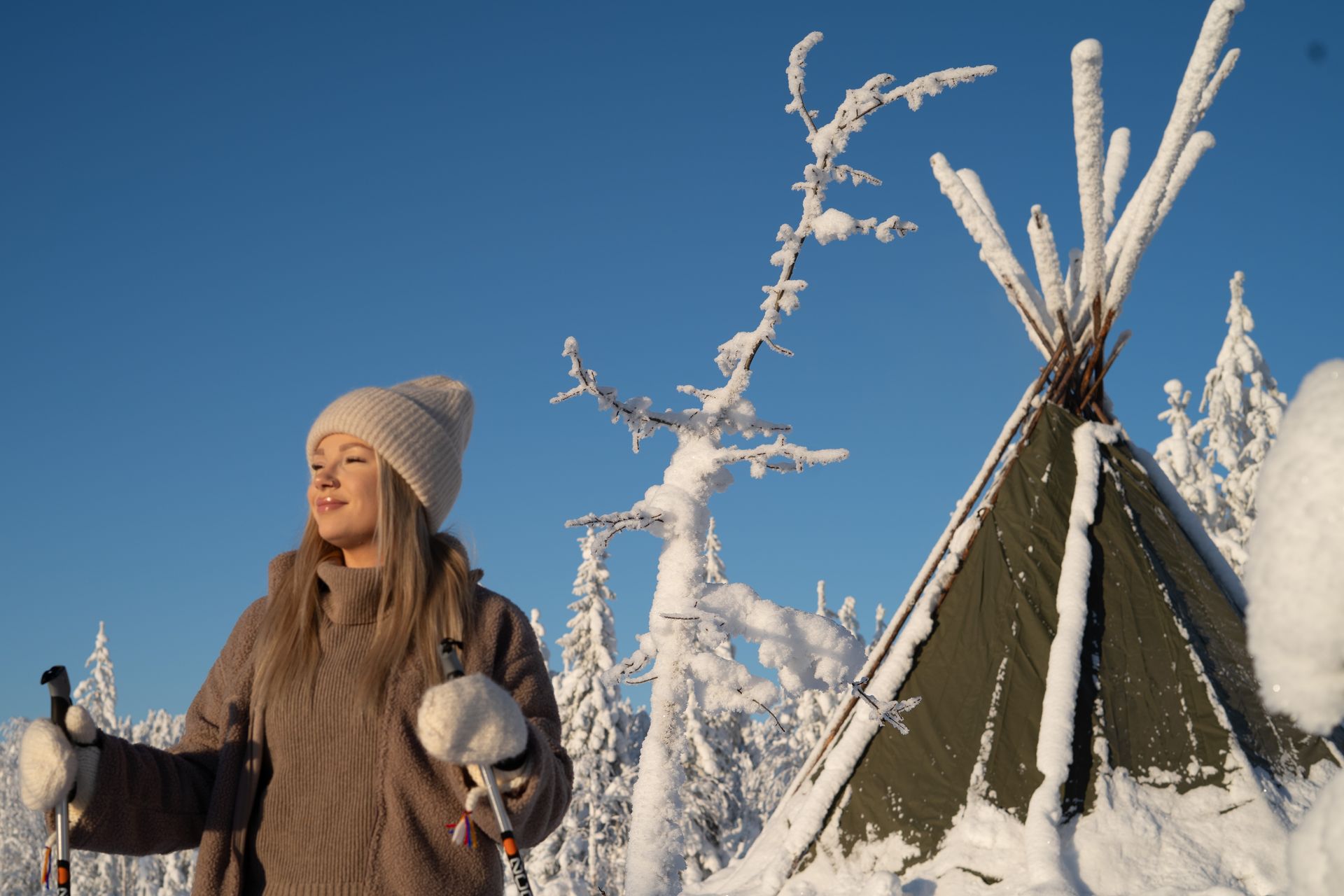 Woman enjoying sunshine in front of a hut and snowy trees.