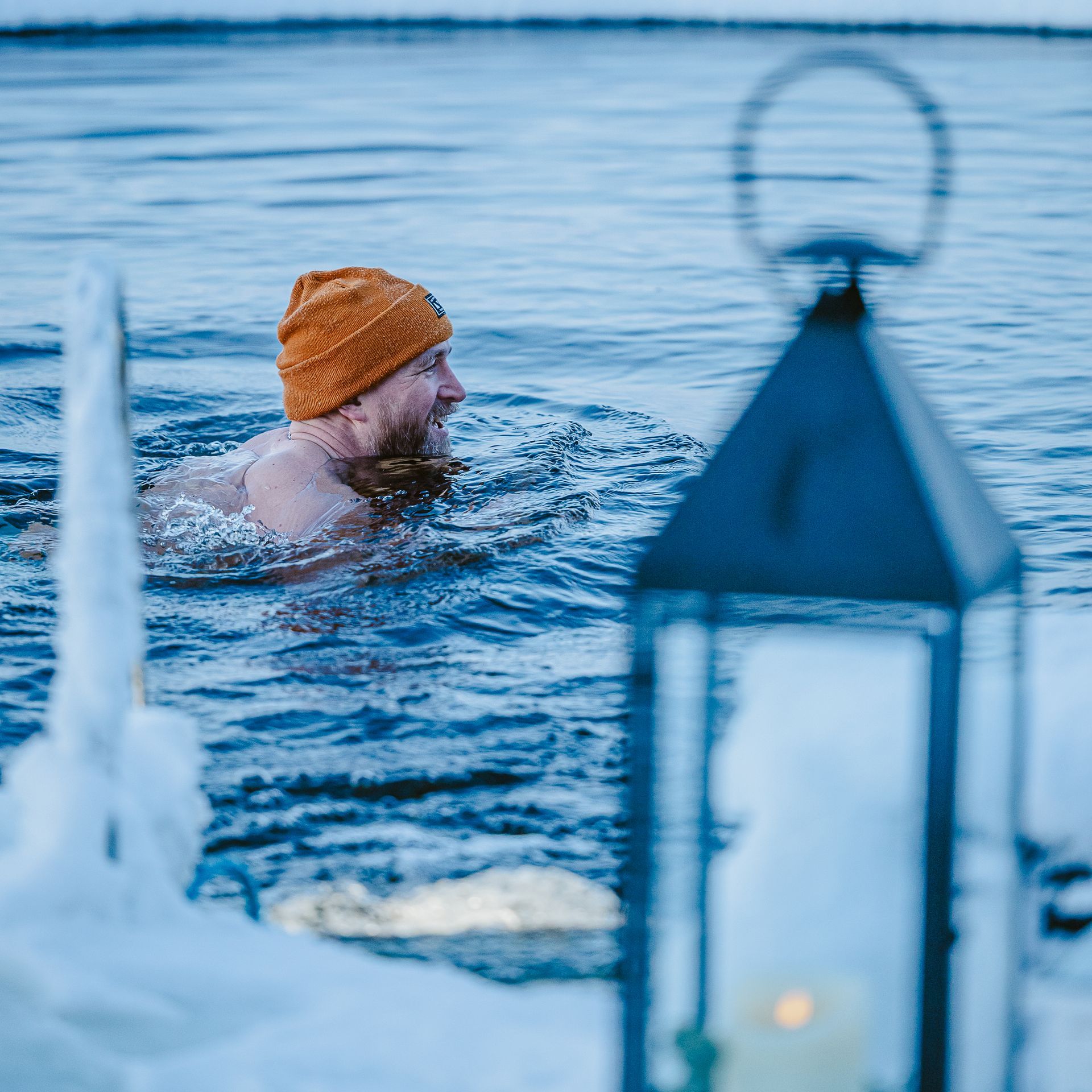 Lantern lit snowy scenery with man swimming in ice hole.