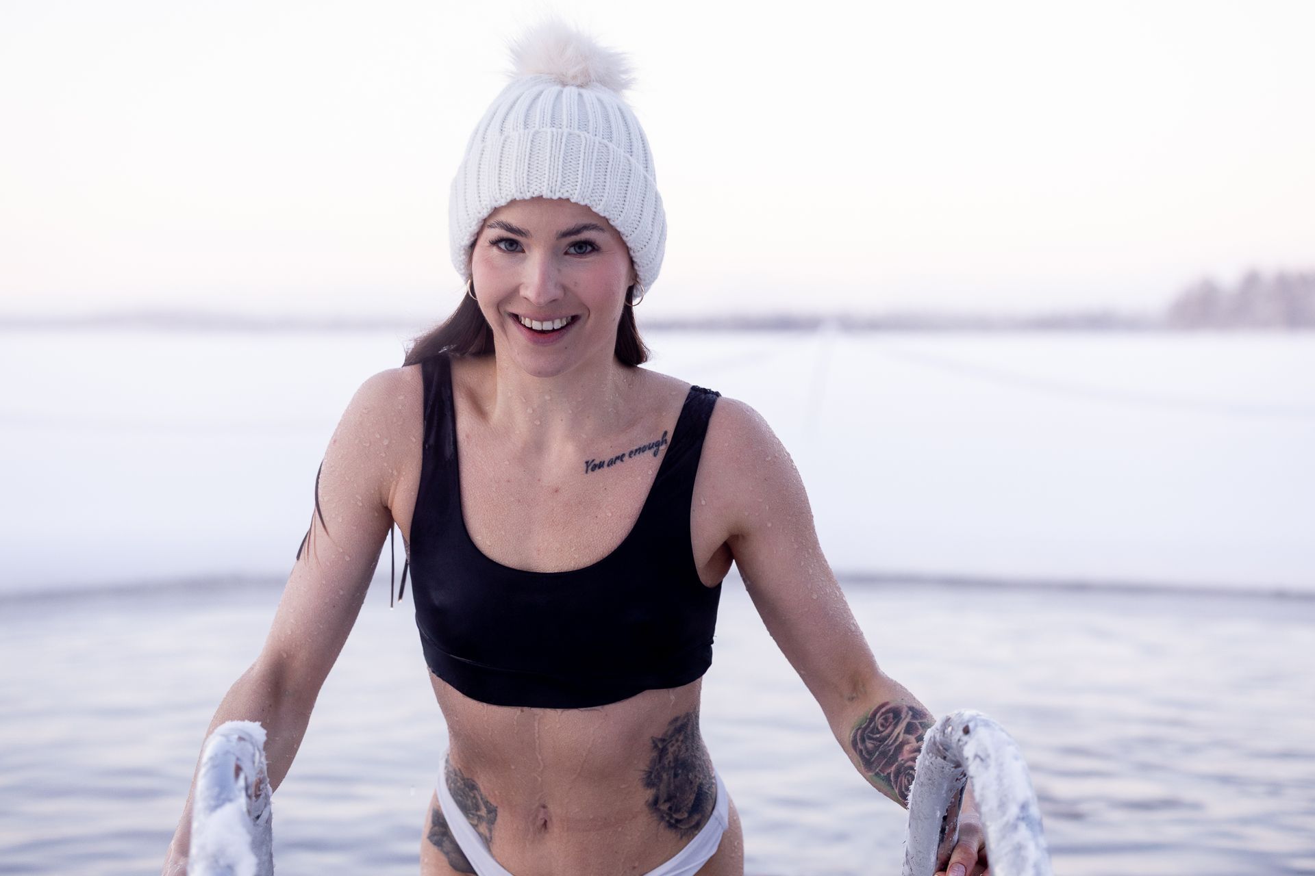 Woman wearing a white wool hat gettin up from ice hole after ice swimming.