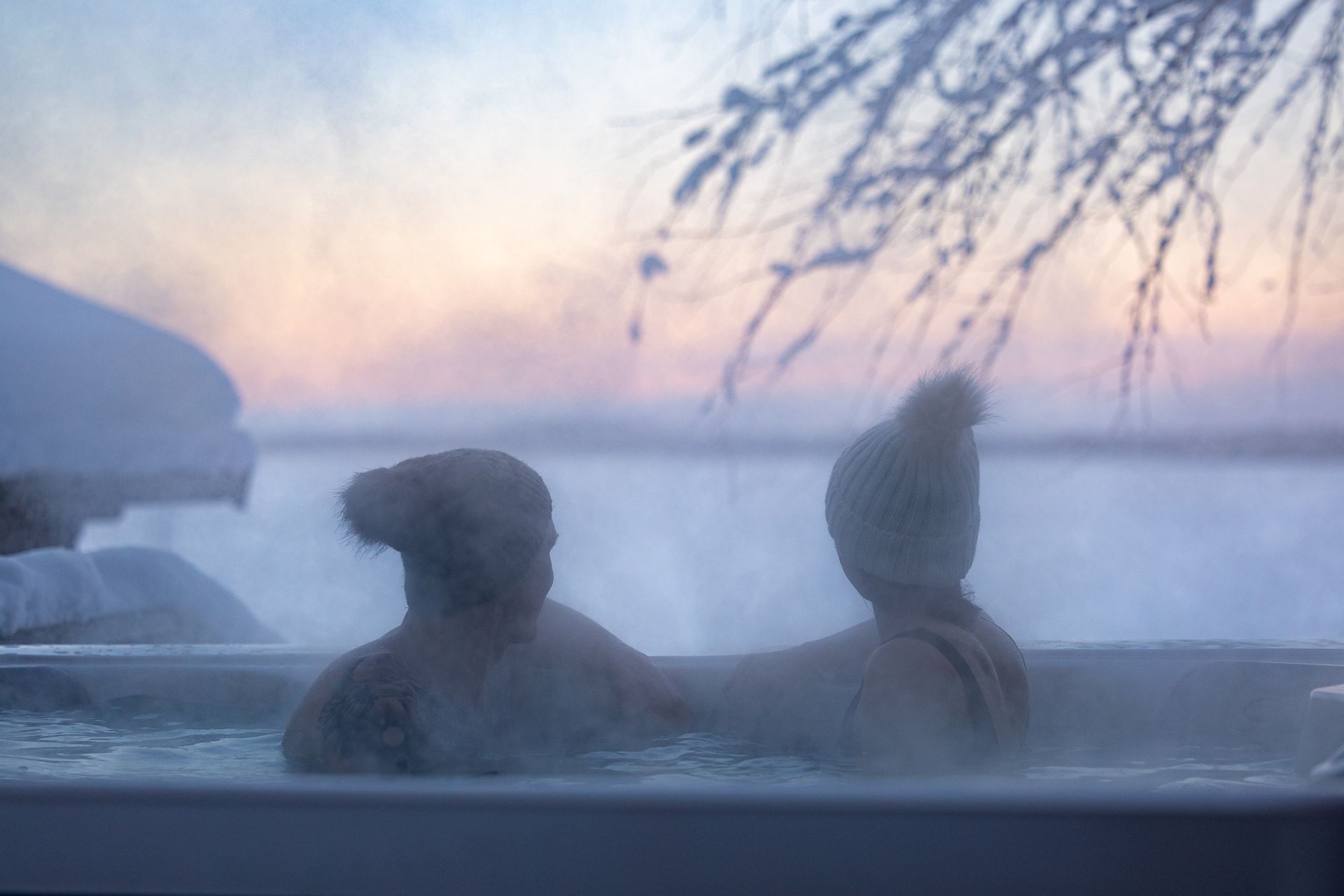 Couple in outdoor hot tub with sun set background.