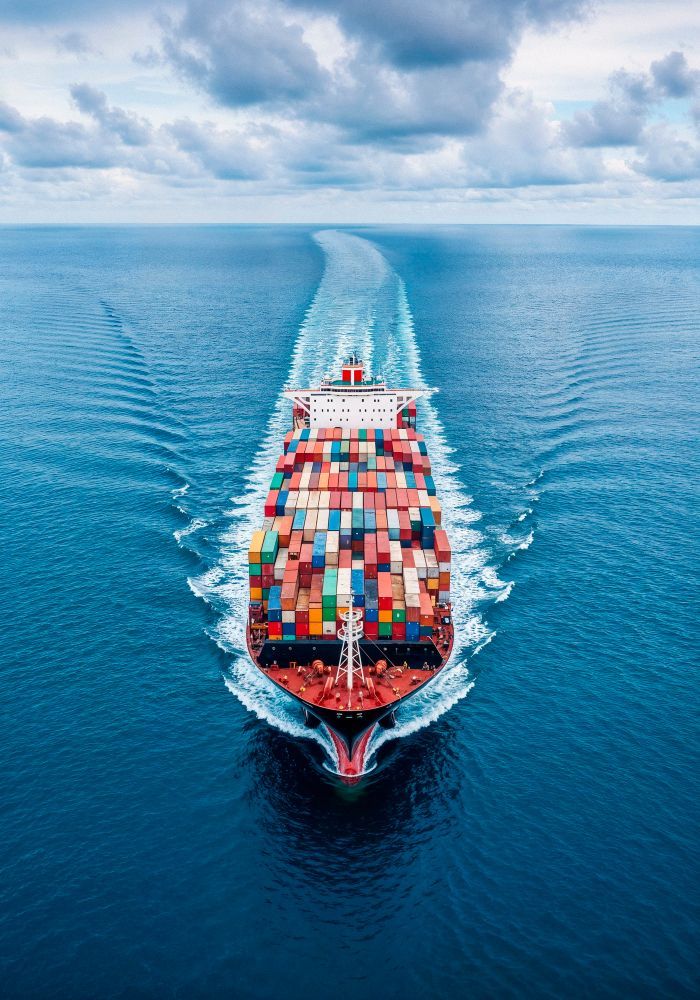 Navio de carga navegando em um mar azul profundo, carregando contêineres coloridos, com um céu nublado acima.