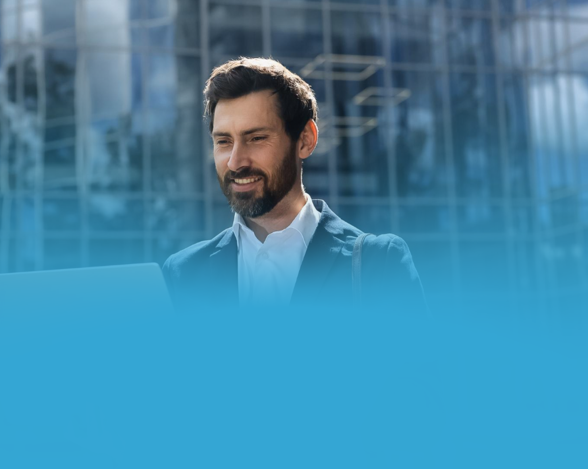 Homem sorridente de terno usando um laptop ao ar livre, com cenário de prédio moderno.