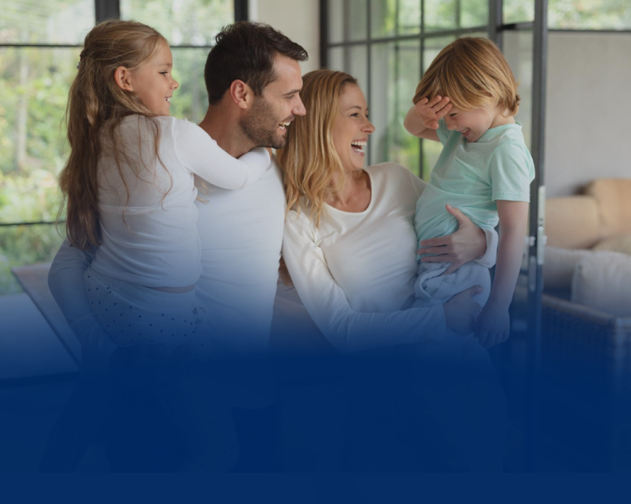 Família de quatro pessoas sorrindo e rindo juntas em um ambiente interno iluminado.