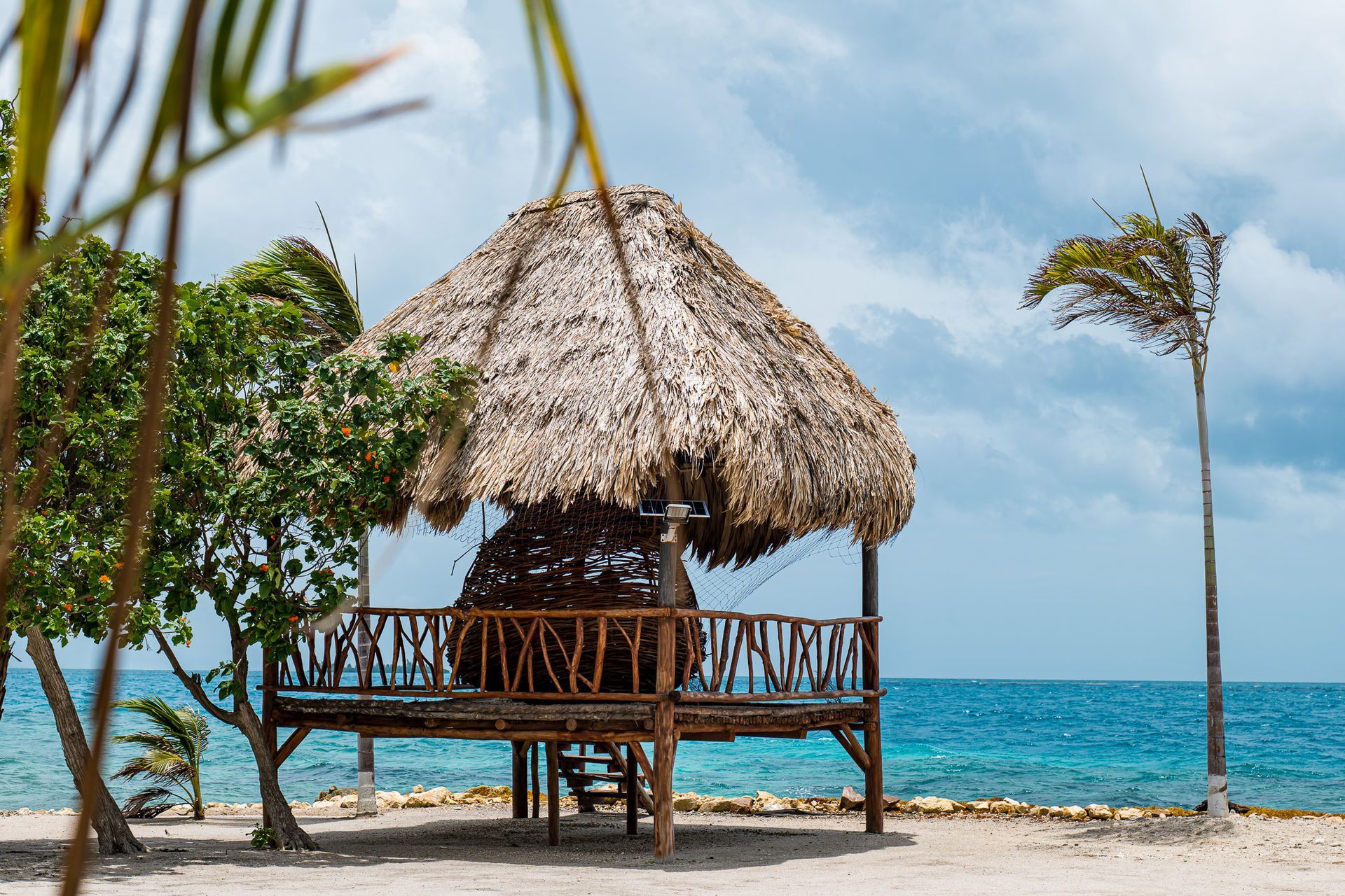 Beach hut with thatched roof overlooking turquoise ocean under a cloudy sky.