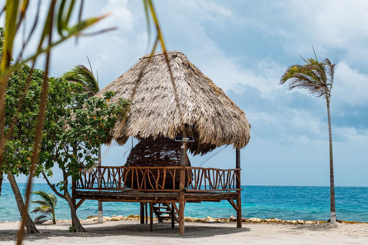 Beachfront hut with thatched roof on a wooden platform; blue ocean, cloudy sky.