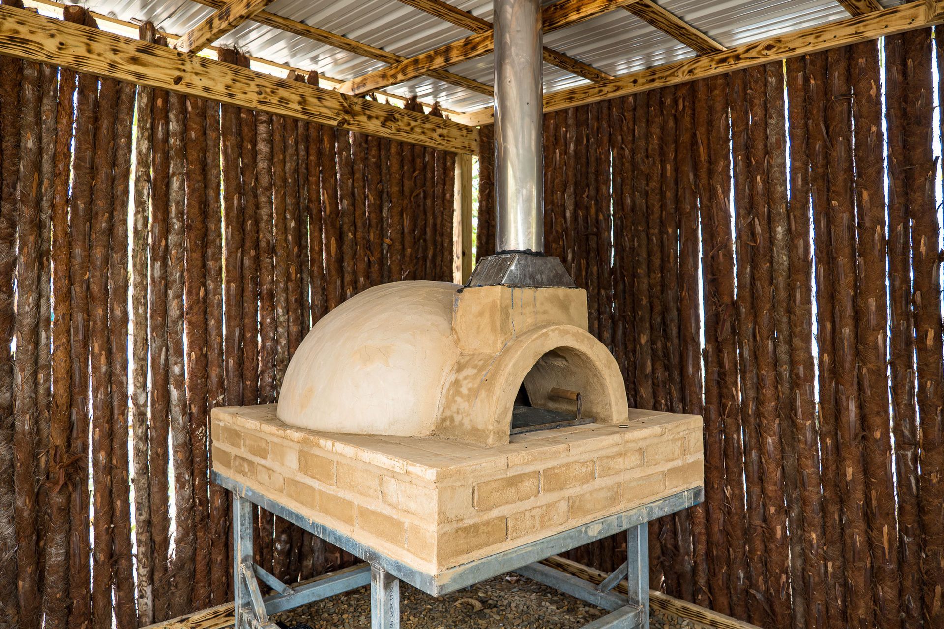 Outdoor brick pizza oven with a metal chimney.