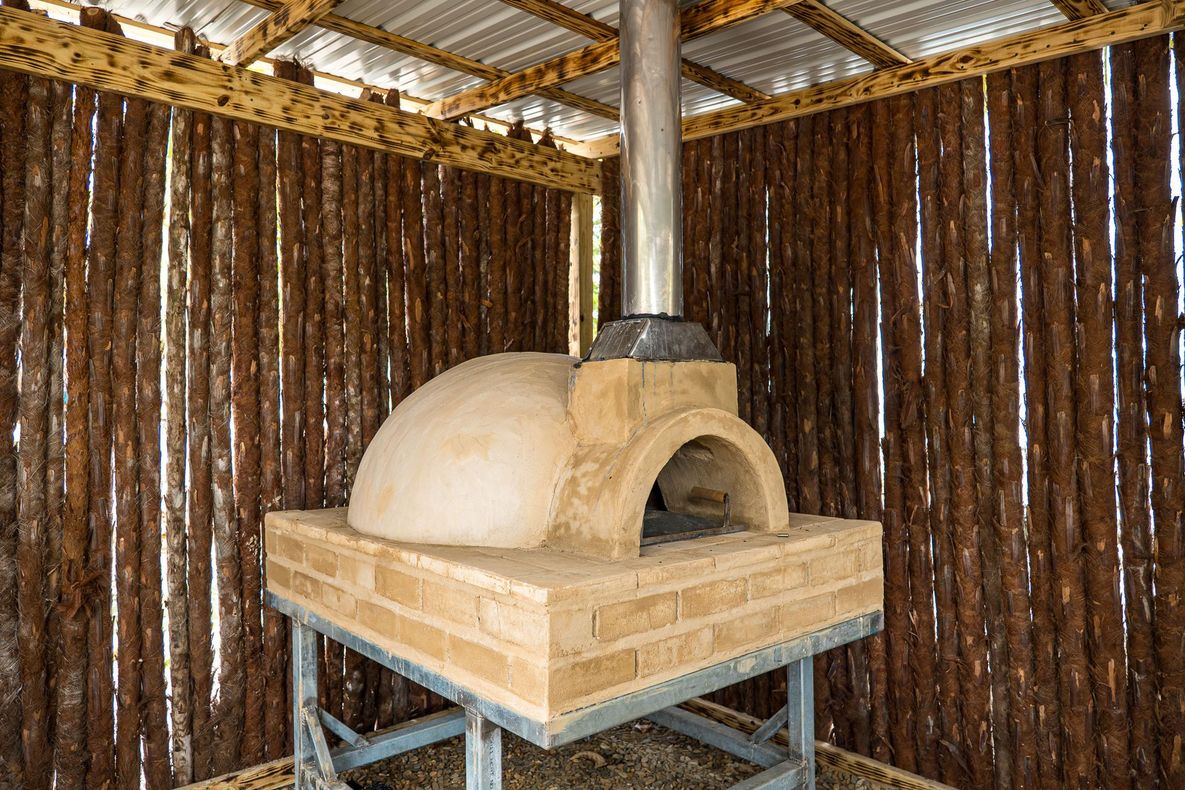 Outdoor brick oven with metal chimney under a wooden shelter.