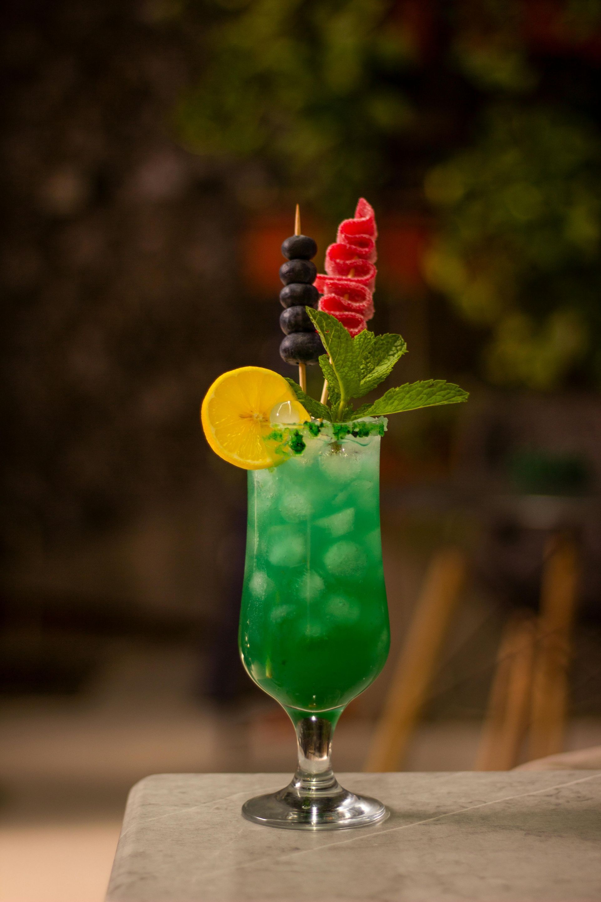 Green cocktail with fruit and mint garnish, set outdoors.