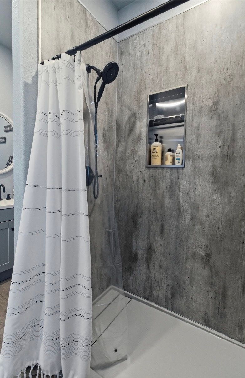 A walk-in shower with concrete-look walls, a matte black rainfall showerhead, and a white, textured fabric shower curtain.