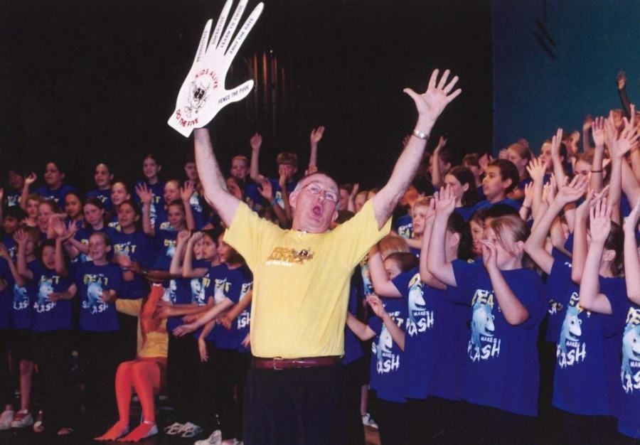 A man in a yellow shirt holds up a hand in front of a choir
