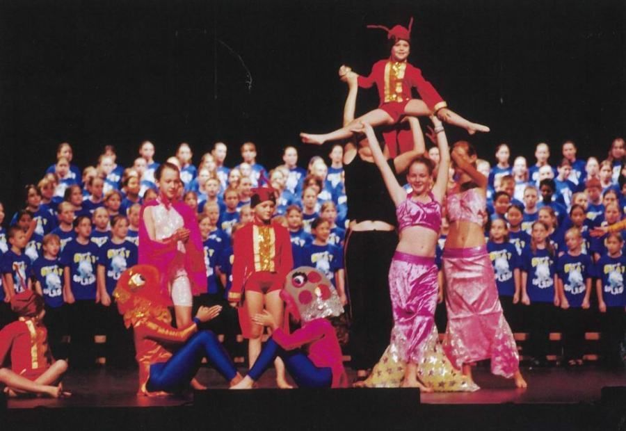 A group of children are performing on a stage in front of a choir