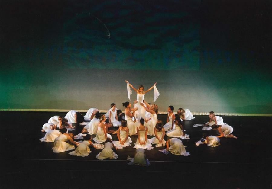 A group of people in white dresses are dancing on a stage