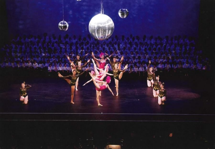 A group of dancers are performing on a stage with a disco ball hanging from the ceiling.