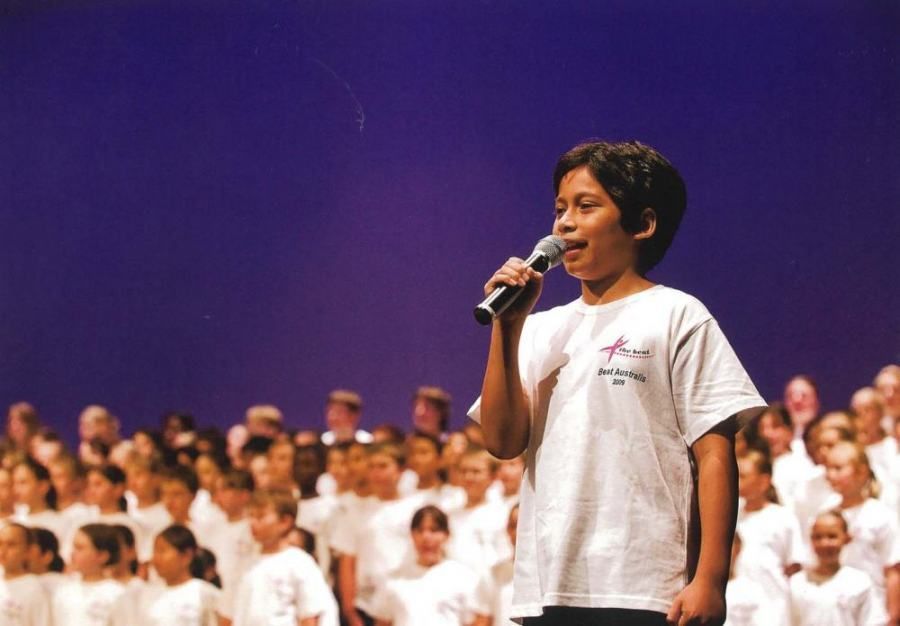 A young boy singing into a microphone in front of a crowd