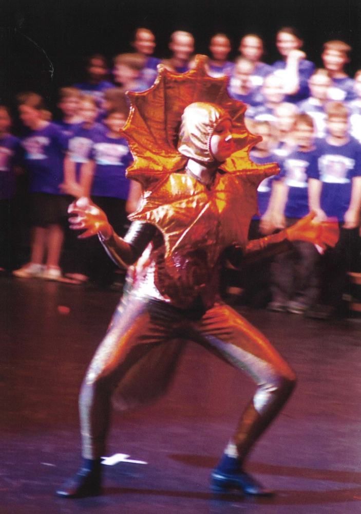 A group of children are watching a person in a dragon costume