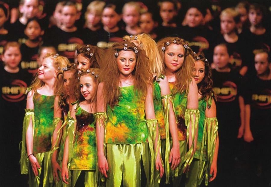A group of young girls are standing in front of a crowd wearing green dresses
