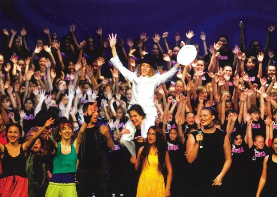 A woman in a white top hat stands in front of a crowd of people