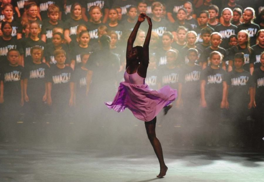 A woman in a purple dress is dancing in front of a large group of children.