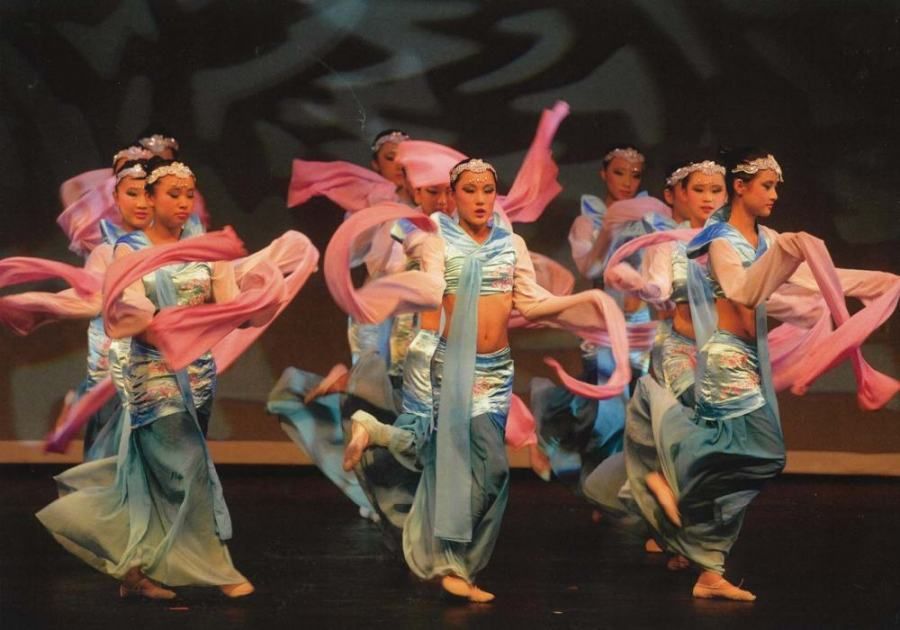 A group of women in blue and pink dresses are dancing on a stage