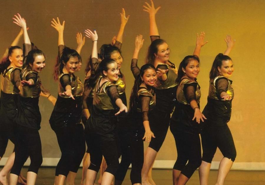 A group of young women are dancing on a stage with their arms in the air