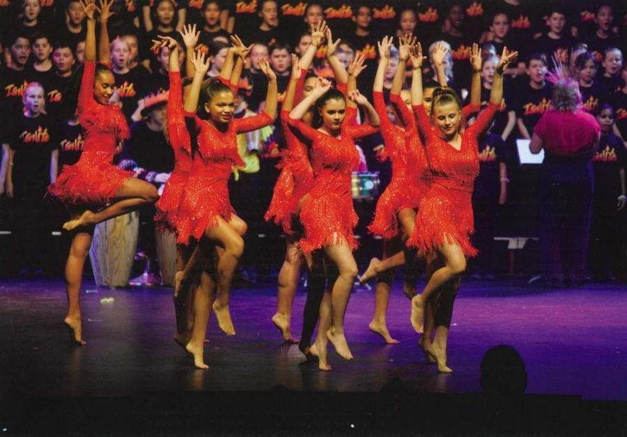 A group of girls in red dresses are dancing on a stage