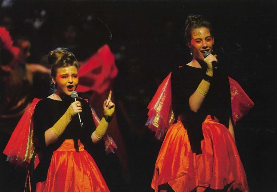 Two women singing into microphones with red paint on their faces