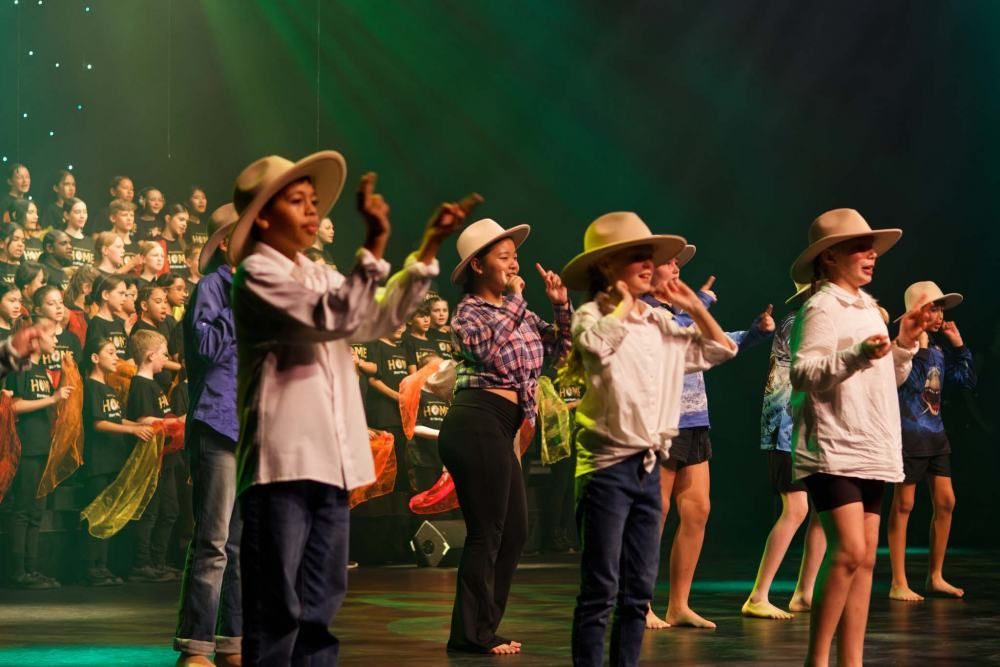 A group of children wearing cowboy hats are dancing on a stage.