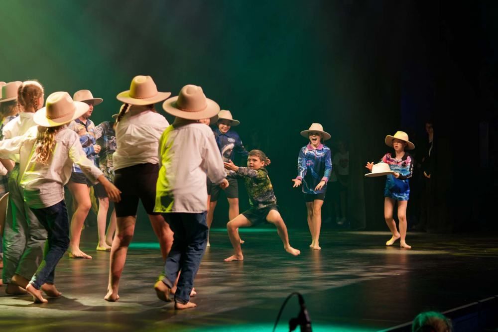 A group of children wearing cowboy hats are dancing on a stage.