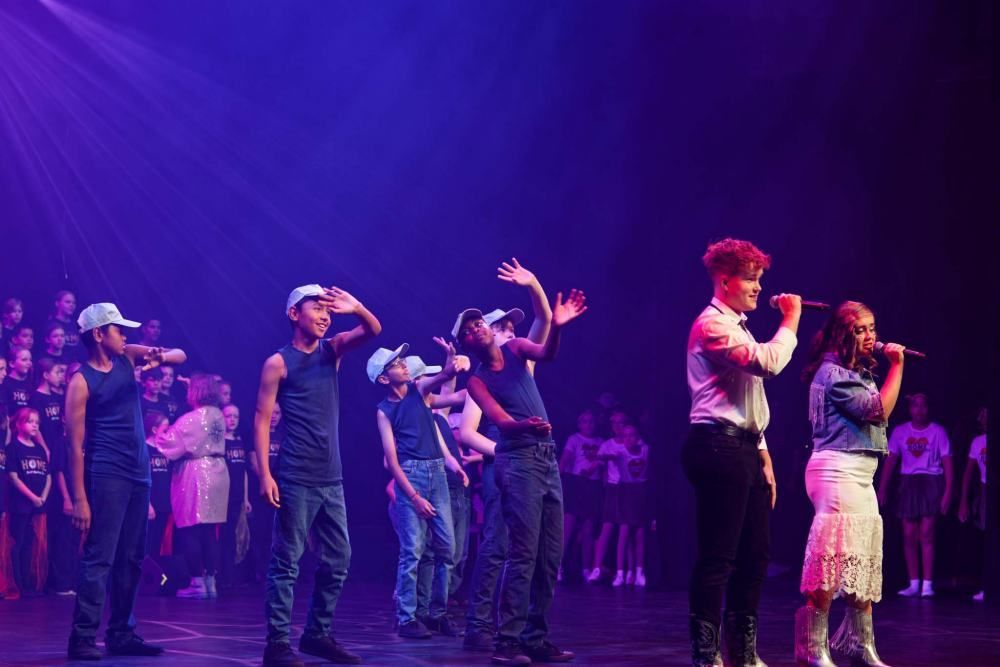 A group of people are standing on a stage singing into microphones.