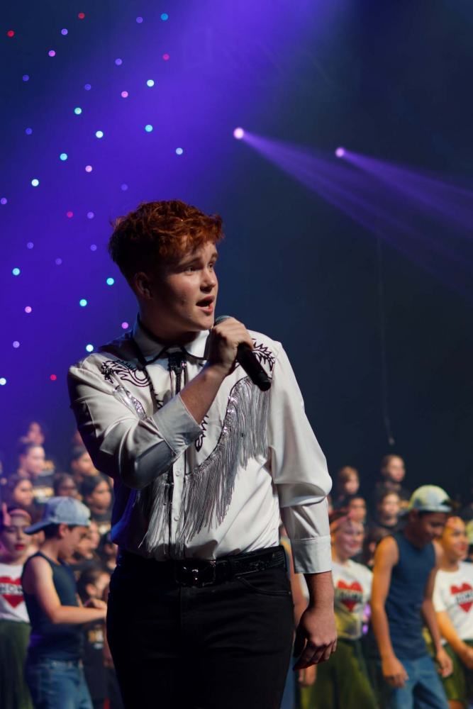 A young man is singing into a microphone on a stage.