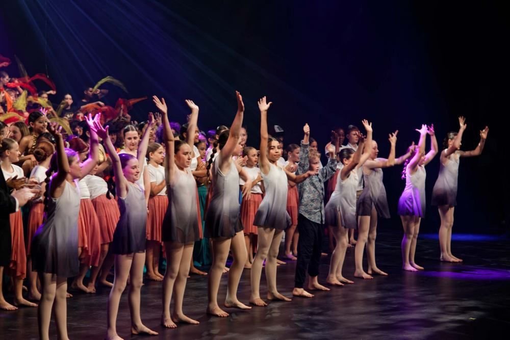 A group of young dancers are standing on a stage with their arms in the air.