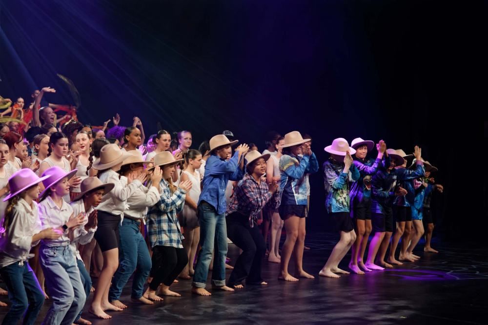 A group of children are dancing on a stage wearing cowboy hats.