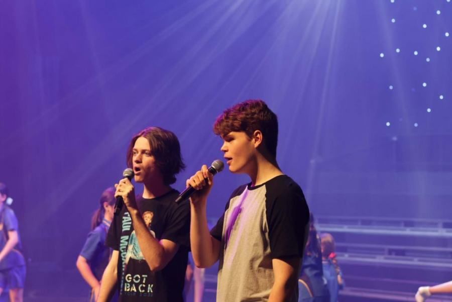Two young men are singing into microphones on a stage.